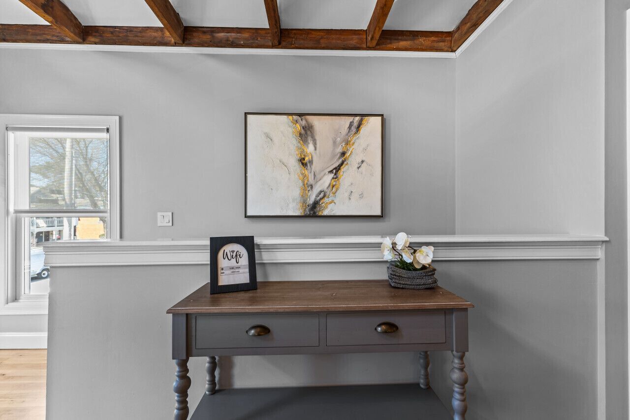 Una habitación con una mesa consola de madera, un cuadro enmarco y un jarrón con flores.
