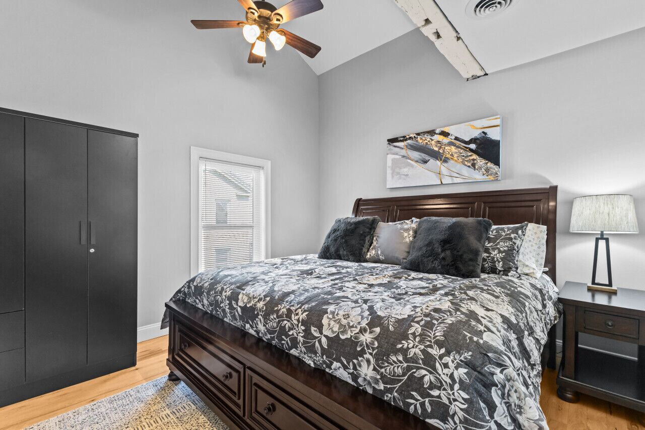 A bedroom with a bed, a ceiling fan, a nightstand, a lamp, and a wardrobe.