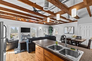 A modern kitchen with a large island, wooden beams, and a dining area with a table and chairs. - Rustic Charm 2BR Downtown Burl. (Burlington)