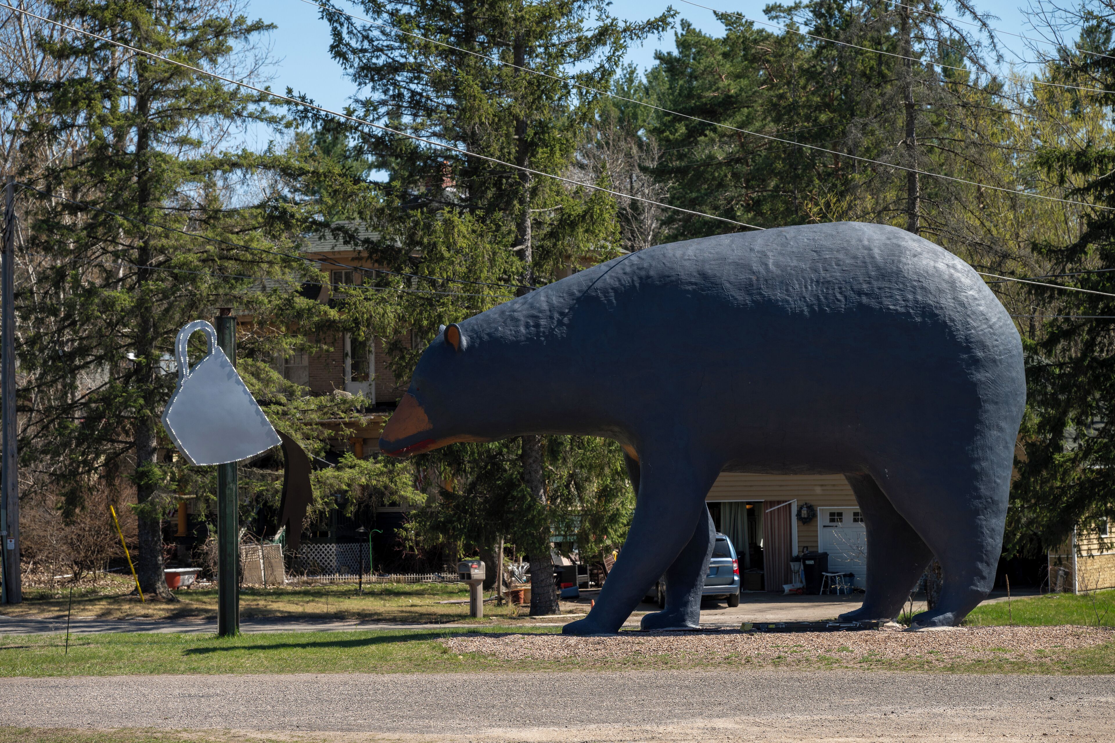 Una gran estatua de oso en un parque, con árboles y un edificio al fondo.