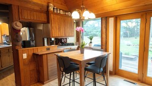 Una cocina de madera con una isla central, taburetes de bar y un amplio ventanal con vistas al exterior.