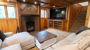 Un salón acogedor con chimenea, televisor grande y una escalera.