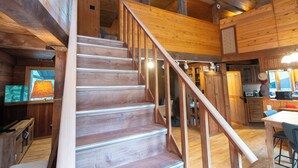 Una escalera de madera que conduce a un segundo piso, una cocina con armarios de madera y una mesa de comedor con sillas.