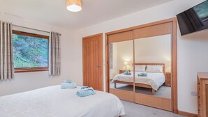 A bedroom with a bed, a mirror, a TV, and a window with curtains. - 5 bedroom accommodation in Nethy Bridge (Nethy Bridge)