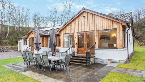 A wooden cabin with a patio, outdoor seating, and a staircase leading to the entrance. - 5 bedroom accommodation in Nethy Bridge (Nethy Bridge)