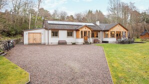 A two-story wooden house with a gravel driveway, a wooden bench, and a table with chairs outside. - 5 bedroom accommodation in Nethy Bridge (Nethy Bridge)