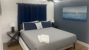 A bedroom with a bed, a ceiling fan, a painting of the sea, and a nightstand with a lamp. - Updated Lakeview condo in Gated community close to beach.  (Destin)