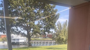 A patio area with a black chair and a small table, a tree, and a view of a dock and water. - Updated Lakeview condo in Gated community close to beach.  (Destin)