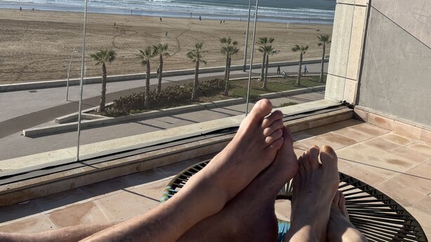 Een balkon met uitzicht op het strand, palmbomen en een heldere lucht.