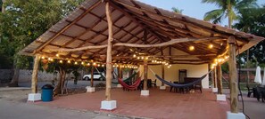 A covered outdoor area with a wooden roof, string lights, a hammock, and a trash bin.