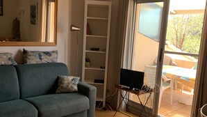 Een woonkamer met een bank, een televisie op een standaard, een boekenkast en een schuifpui naar een buitenruimte.