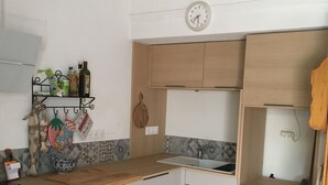 Een kleine keuken met witte kastjes, een houten aanrecht, een spoelbak en een klok aan de muur.