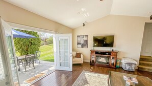 Un vaste espace de vie comprenant une porte-fenêtre coulissante donnant sur un patio, un canapé confortable, une table basse et un téléviseur.