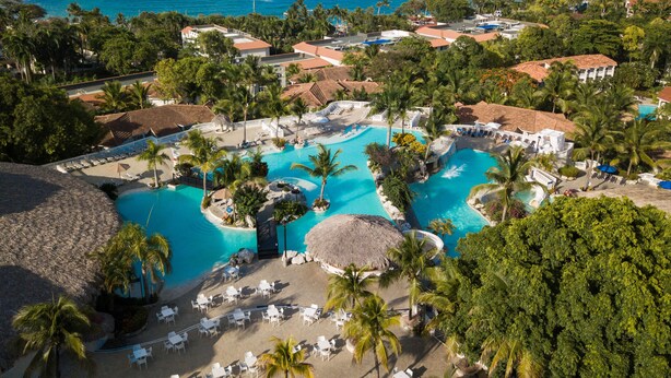 Un complexe hôtelier doté d’une grande piscine centrale, de plusieurs petites piscines et d’une plage aménagée avec des chaises longues.