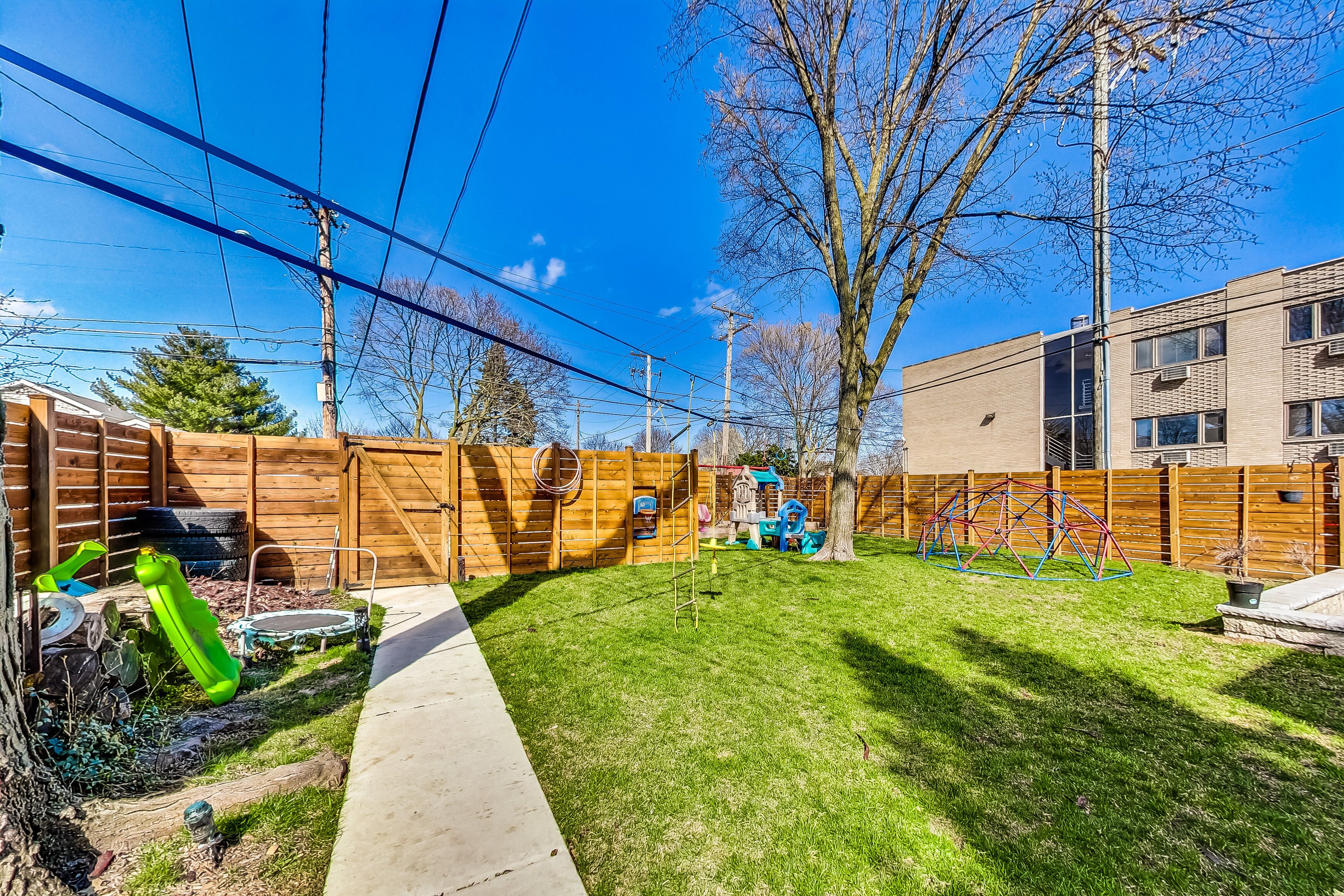 A backyard with a wooden fence, a trampoline, and a play structure.