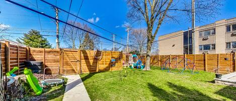 A backyard with a wooden fence, a trampoline, and a play structure.