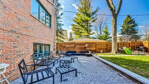 Une terrasse extérieure avec un sol en briques, des meubles en métal et une clôture en bois.