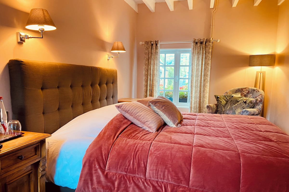 A bedroom with a large bed, a nightstand, a chair, and two wall-mounted lamps.