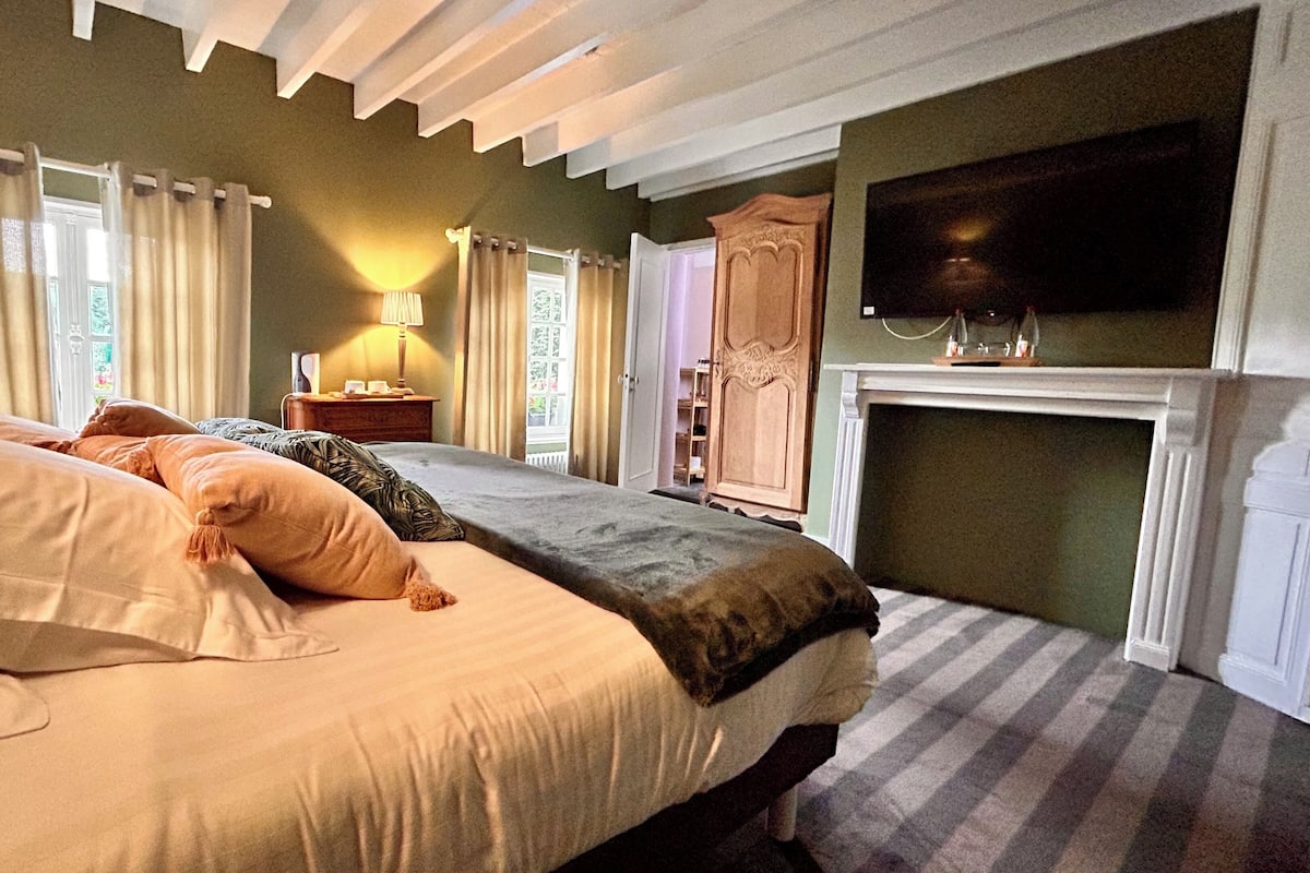A bedroom with a large bed, a fireplace, and a television on the wall.
