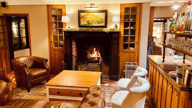 Un espacio lounge acogedor con chimenea, asientos de cuero, una mesa de centro de madera y un bar con botellas y copas.