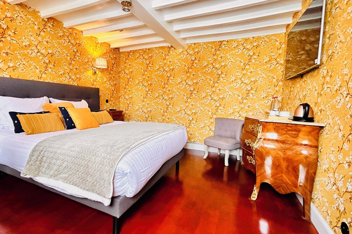 A hotel room with a large bed, a dresser, a chair, and a mirror on the wall.