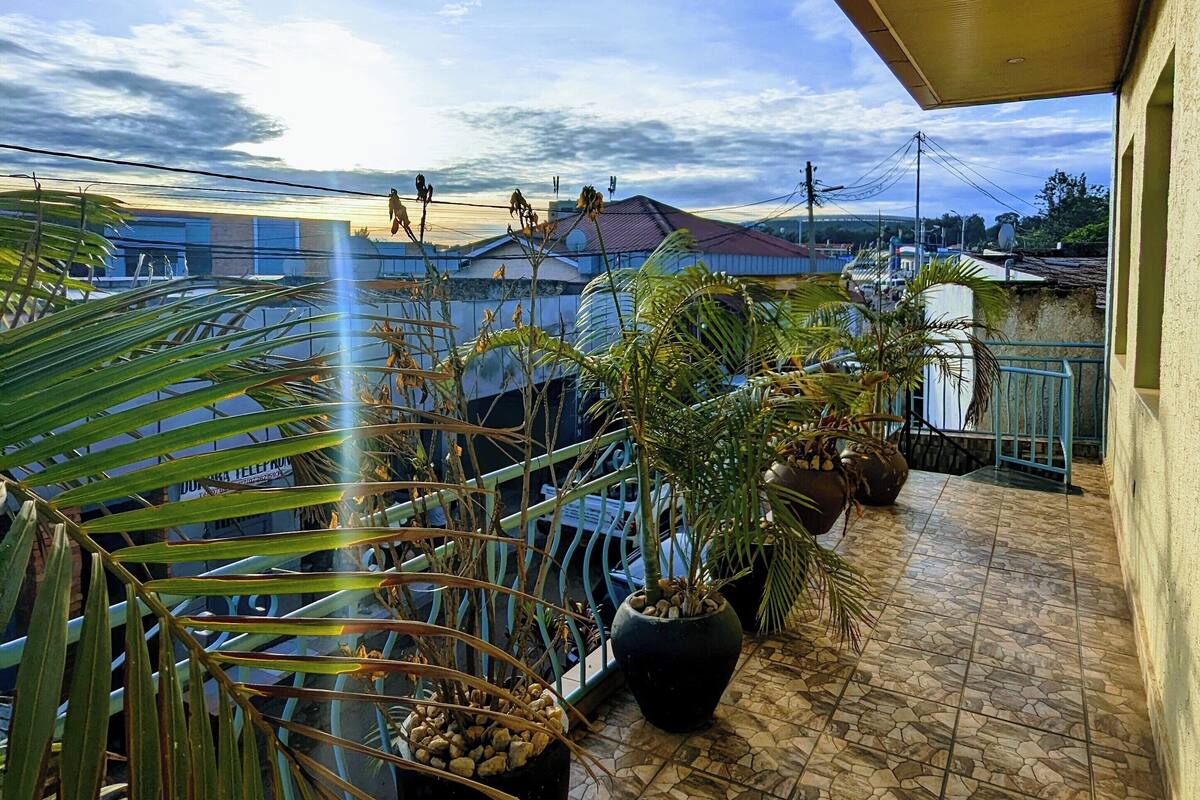 A terrace with potted plants, a tiled floor, and a view of buildings in the distance.