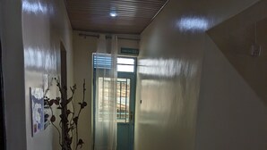 A hallway with a wooden floor, a door with a window, and a plant. - URBAN VIBER MOTEL (Kigali)