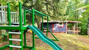 A playground with a green slide and climbing structure, surrounded by trees and a small building. - Unplug & Recharge at Whispering Pines Ringgold (Malta)