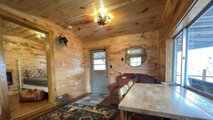 A wooden cabin interior with a bed, a sofa, a dining table, and a patterned rug. - Unplug & Recharge at Whispering Pines Ringgold (Malta)