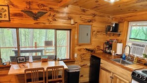 A wooden cabin interior with a dining area, kitchen, and large windows overlooking a forest. - Unplug & Recharge at Whispering Pines Ringgold (Malta)