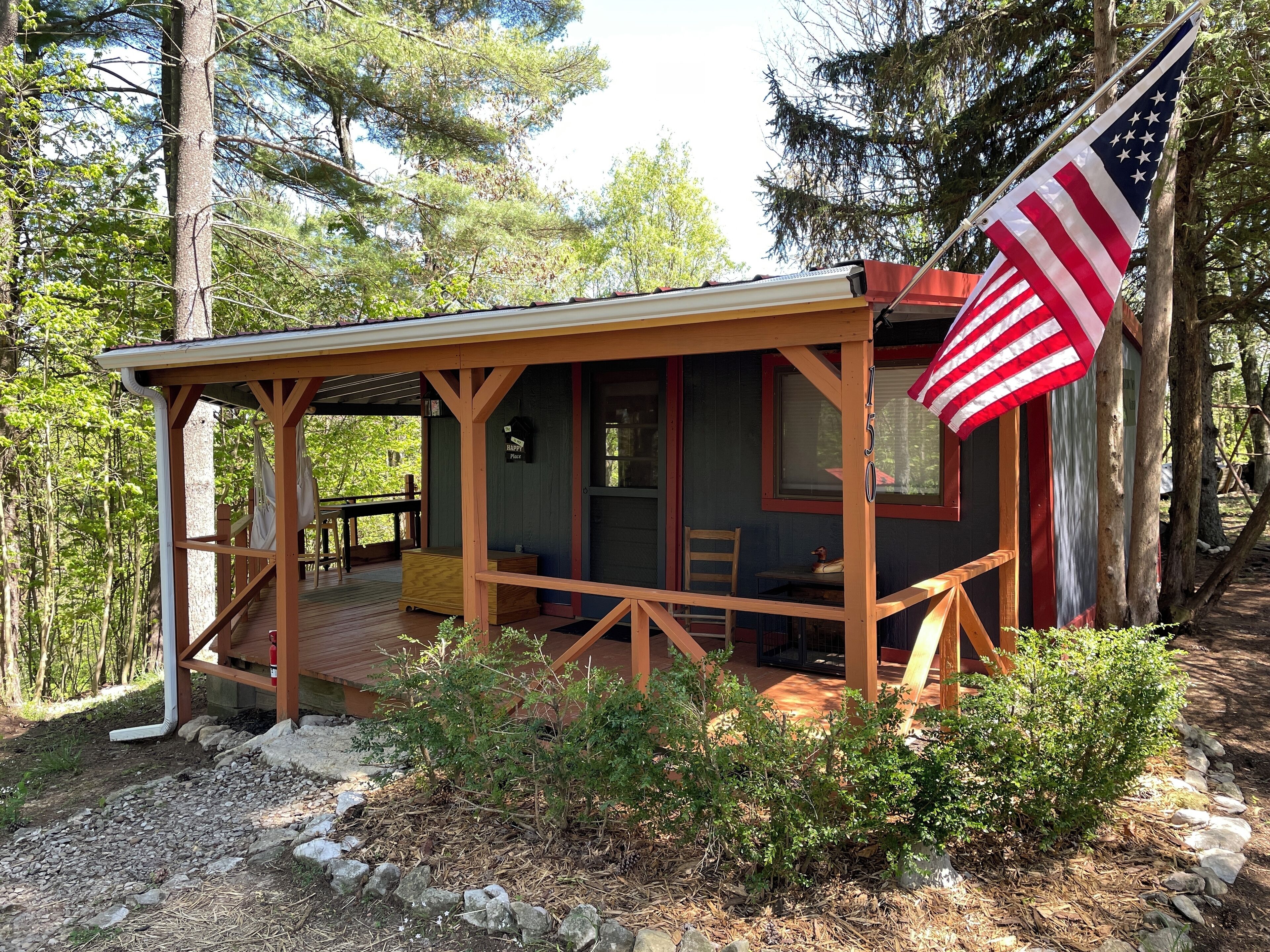 A rustic cabin with a porch, a small table, and a flag.