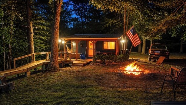 A cabin with a fire pit, an American flag, and a car parked nearby. - Unplug & Recharge at Whispering Pines Ringgold (Malta)