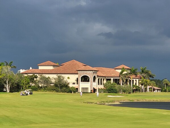 A large, multi-story building with a central entrance, surrounded by a well-maintained lawn and palm trees.