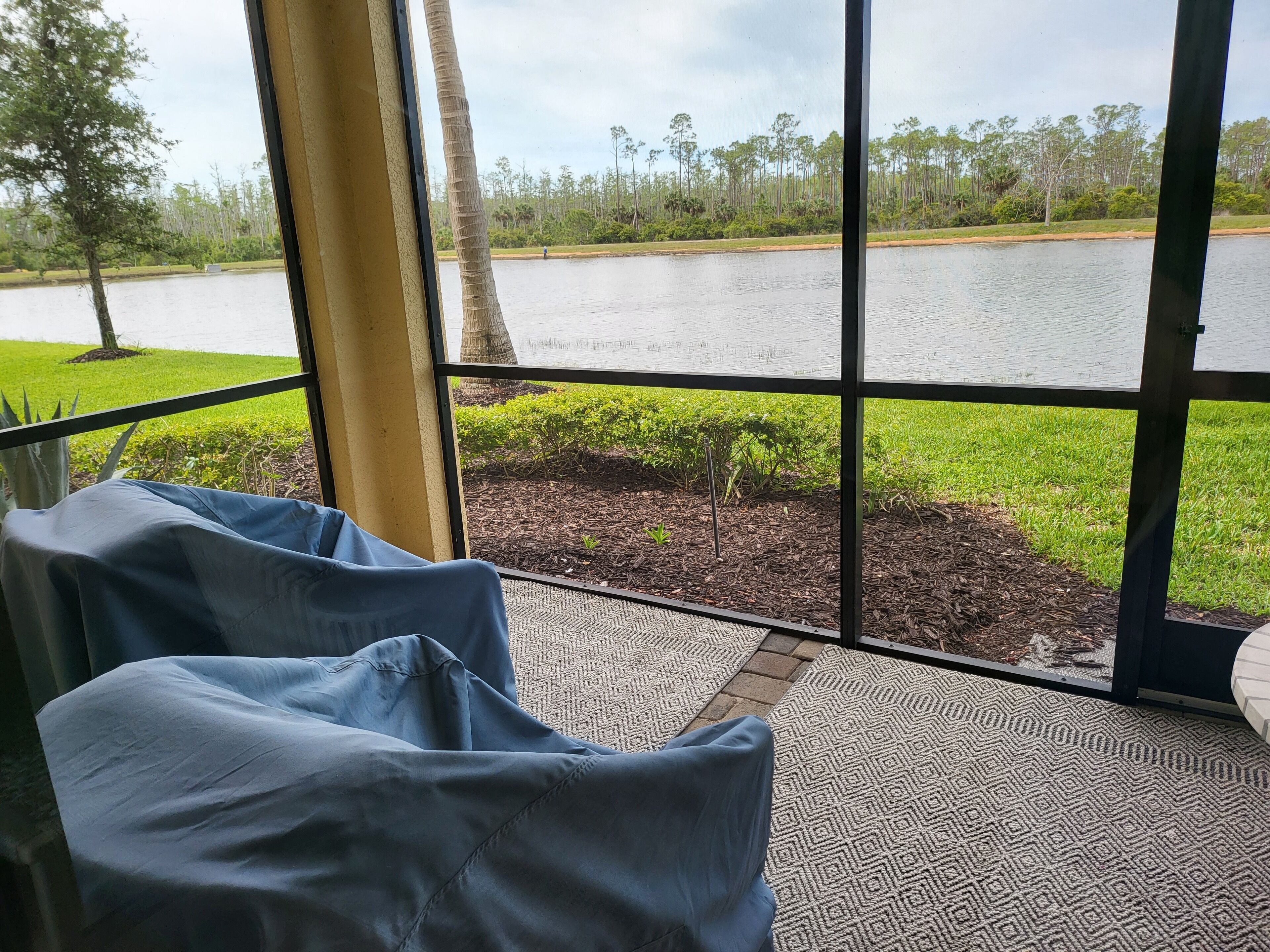Una habitación con un ventanal grande que da a un lago, un pequeño jardín y una silla azul.