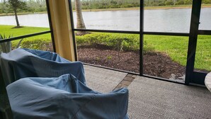 Une pièce dotée d’une grande fenêtre donnant sur un lac, d’un petit jardin et d’une chaise bleue.