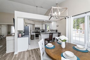 A spacious kitchen with white cabinetry, a central island, and a dining area with a wooden table set for four. - Castle Glow - 2BR - BBQ Gr - Walk to Kroger Field (Lexington)