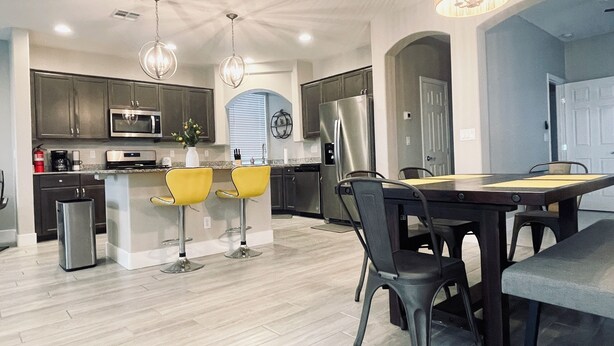A modern kitchen with a central island, bar stools, a dining table with chairs, and a refrigerator. - Best 3-Story Home in Vegas - 9mins to Everything! (Las Vegas)