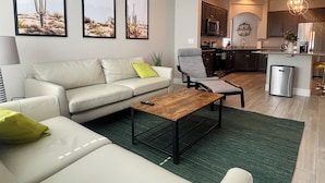 A modern living room with a sofa, armchair, and coffee table, a kitchen with cabinets and appliances, and desert-themed wall art. - Best 3-Story Home in Vegas - 9mins to Everything! (Las Vegas)