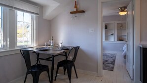 A dining area with a table set for two, two chairs, a wine bottle, and glasses. There is a window with blinds, a ceiling fan, and a shelf with decorative items. - Freshwater Flat, Downtown Douglas - Apart in Downtown right off Center Street. (Douglas)