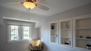 A room with a ceiling fan, a window with blinds, a chair with a map pattern, and built-in shelves with decorative items. - Freshwater Flat, Downtown Douglas - Apart in Downtown right off Center Street. (Douglas)