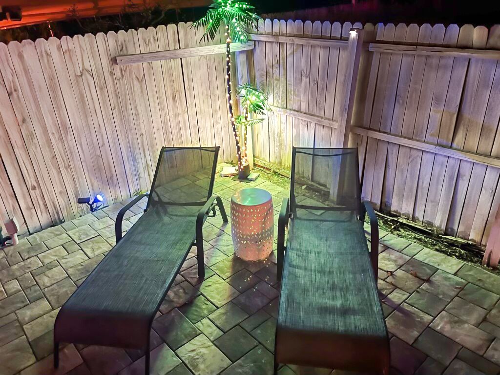 Eine Terrasse mit zwei Metallstühlen und einem kleinen Tisch, umgeben von einem Holzzaun und einer mit Lichtern verzierten Palme.