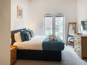 Quarto com cama, mesa de cabeceira, penteadeira, televisão e porta de vidro deslizante para área externa.