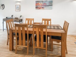 Zona pranzo con tavolo e sedie in legno, un quadro appeso al muro e un piccolo tavolino con una ciotola e una pianta.