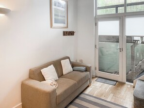 A neutral-toned living room with a beige sofa, two white cushions, and a framed picture on the wall.