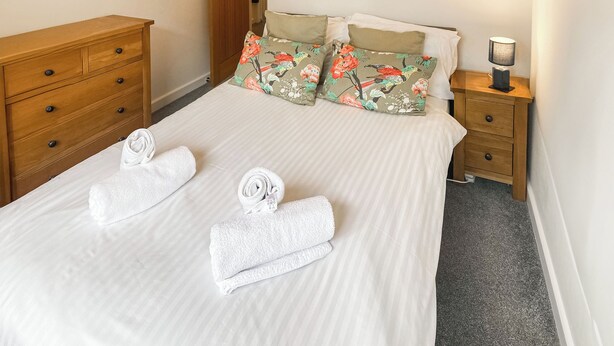 A neatly made bed with white linens and two rolled towels placed on it.