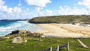 A coastal landscape with a beach, rocky outcrops, and grassy hills.