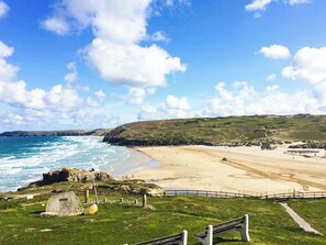 A coastal landscape with a beach, rocky outcrops, and grassy hills.