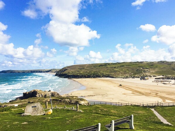A coastal landscape with a beach, rocky outcrops, and grassy hills.