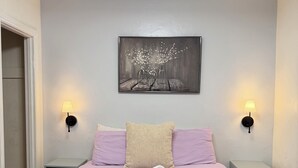 Una cama bien hecha con una paleta de colores rosa y blanco, dos mesitas de noche con lámparas, un cuadro sobre la cama y una puerta a la izquierda.