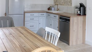 A modern kitchen with a wooden table, white cabinets, a stone accent wall, and a built-in dishwasher. - Mas Provençal Rénové Luberon (La Bastide-des-Jourdans)